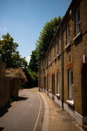 Chiswick, London, UK â 2025.06.13: A peaceful, narrow residential street lined with classic Victorian brick terraced houses under a bright summer sky, surrounded by lush green trees.の写真素材