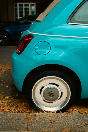 Chiswick, London, UK â€“ 2025.07.09 â€“ Close-up of the rear quarter of a turquoise Fiat 500 with retro wheel design and scattered autumn leaves on the pavement
