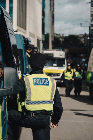 London, UK â€“ 2025.09.13 â€“ A police officer in a high-visibility vest marked â€œPOLICEâ€ stands by riot vans while monitoring and securing the route during a free speech protest.