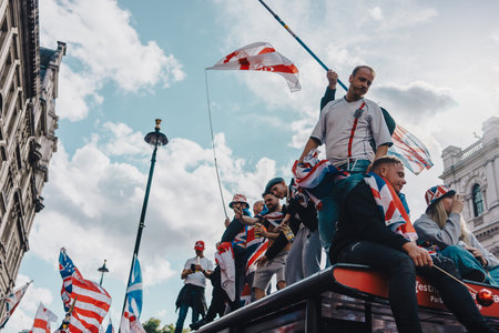 London, UK â€“ 2025.09.13 â€“ A group of protesters wave flags and stand on top of a bus during a Free Speech protest in Westminster. Demonstrators display Union Jack and St. Georgeâ€™s flags under a cloudy sky.