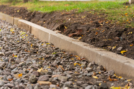 In this tranquil setting, a new gravel path emerges, meticulously edged by a sturdy concrete curb, while vibrant leaves scatter across the ground, inviting exploration.の写真素材