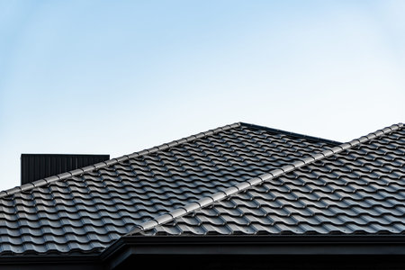 Two intersecting rooftops featuring textured tiles rise under a bright blue sky, emphasizing modern...