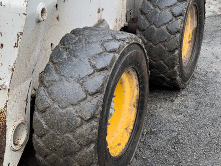 The heavy-duty tires of a bobcat are covered in mud, highlighting their use in a construction environment. The ground is gravelly and worn from activity throughout the day.の写真素材