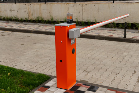 The bright orange barrier arm is installed at a parking lot entrance, designed to manage vehicle...