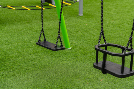 At this lively playground, two swings await eager children, set against a backdrop of soft grass,...