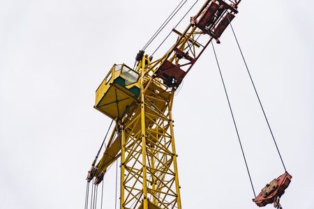 The bright yellow crane dominates the skyline, its operator carefully maneuvering materials for an ongoing construction project as clouds roll by above.の写真素材