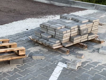 Stacked paving bricks rest on wooden pallets at a construction site where a sidewalk is being laid. Various materials are scattered around, indicating ongoing work.の写真素材