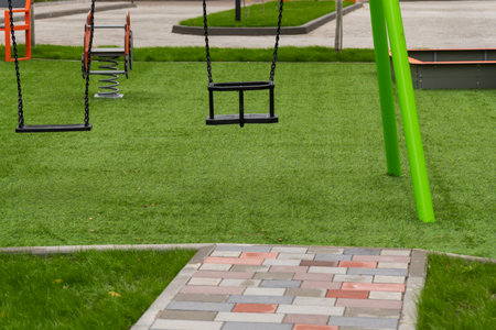 Swings in a vibrant public park invite children to experience the joys of childhood. The green grass and sunny atmosphere enhance the playful environment for outdoor fun.の写真素材
