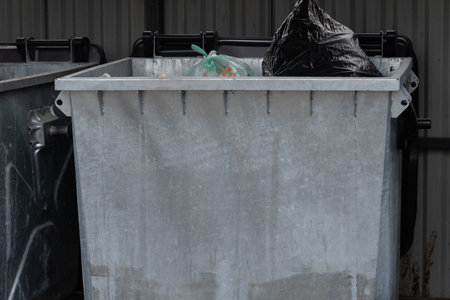A metal garbage container overflowing with trash underscores the importance of waste management and recycling for promoting environmental sustainability in urban areas.の写真素材