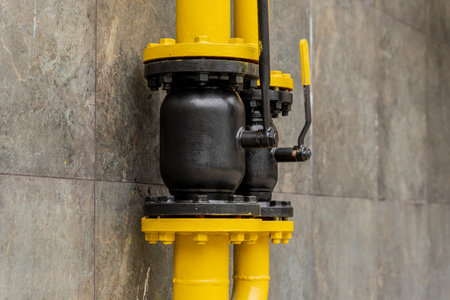 A yellow gas pipe with a black valve is mounted on a grey wall, showcasing an essential connection for transporting gas. The setup reflects modern energy infrastructure.の写真素材