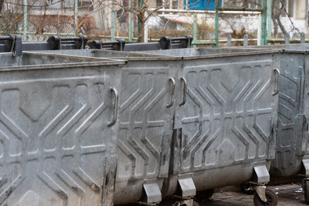 Rows of metal garbage containers filled with trash bags stand in an urban setting, highlighting the...