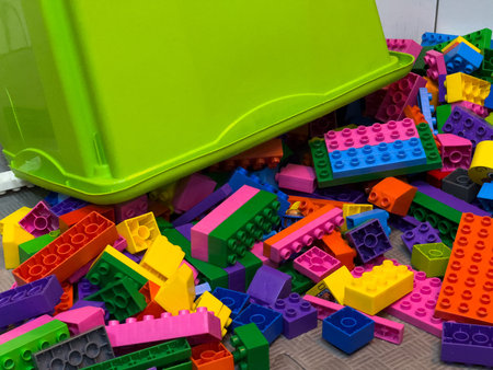 Colorful plastic building blocks are strewn across the floor, surrounding an overturned green...