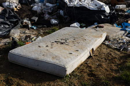 Discarded mattresses and various trash clutter a landfill, showcasing the critical issue of waste management and environmental impact.の写真素材