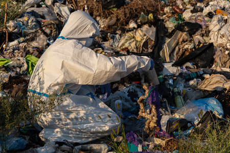 An environmental worker in protective gear is sorting through trash in a landfill during sunset, aiming to clean up plastic waste.の写真素材