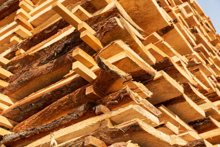 Wooden planks are neatly stacked and drying under the bright sunlight at a lumber yard in the...