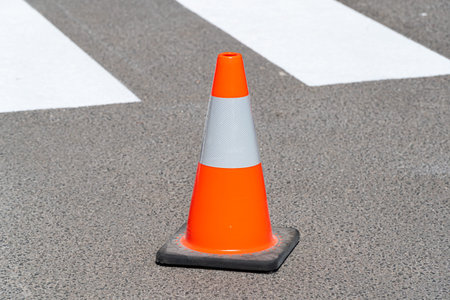 Traffic cone, with white and orange stripes on gray asphalt. Construction cone. Symbol of...