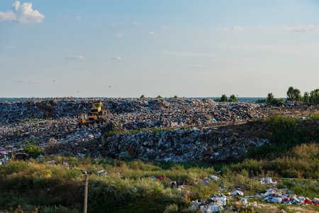 Heavy machinery is clearing sections of a landfill filled with garbage and plastic debris, highlighting pollution issues in this area.の写真素材