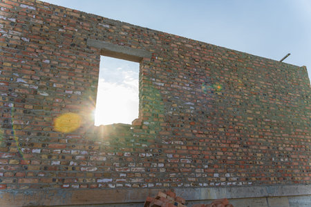 Bright sunlight shines through an unfinished window in a brick wall, indicating progress in a...