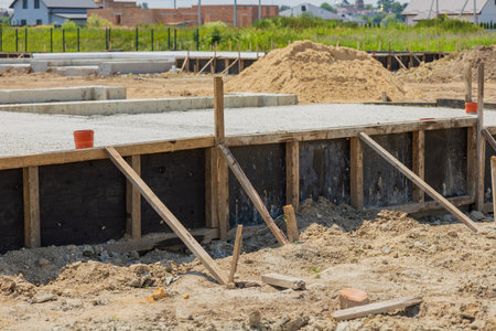 Workers are preparing a concrete foundation for a new residential building, with wooden supports...