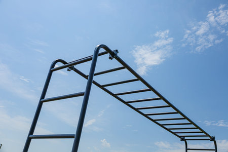 Gymnast engages in strength training on horizontal parallel bars under a clear blue sky,...