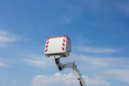 A tall work platform is lifted high, showcasing its reach against a bright, sunny sky with scattered...