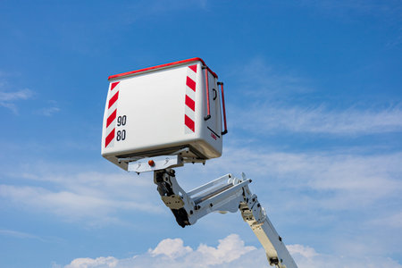 Construction workers utilize a raised platform for maintenance tasks in an open area under clear skies and bright sunlight.の写真素材