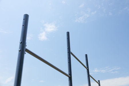 Vertical bars create a workout station for users in a serene park setting under a bright sky with...