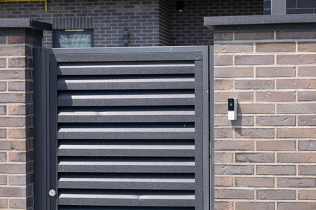Sleek black slatted door stands closed at an urban home entrance, featuring a security device...