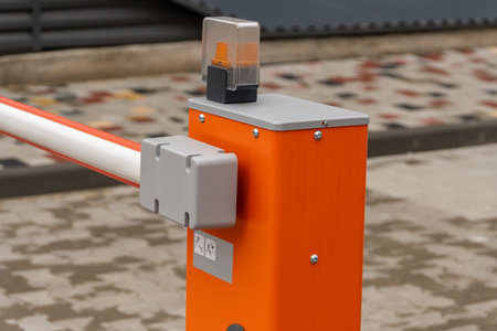 Orange parking gate: barrier, mechanism, flashing light on paved lot.