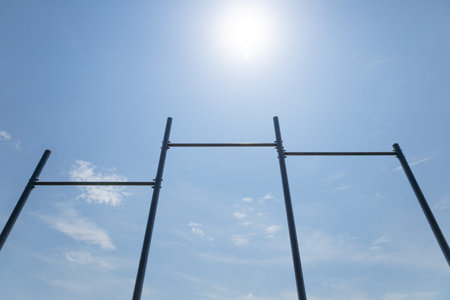 Metal bars rise toward a bright sun, casting shadows on a clear blue sky, symbolizing outdoor...