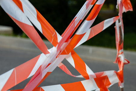 Bright warning tape in orange and white creates a barrier around a construction site in the city during daylight hours, signaling caution.の写真素材