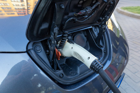 Electric vehicle is being charged at a charging station in a city area with buildings in the background under clear skies.の写真素材