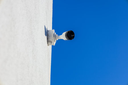 A security camera is installed on a white structure, angled toward a vibrant blue sky, ensuring a watchful eye on its surroundings.の写真素材