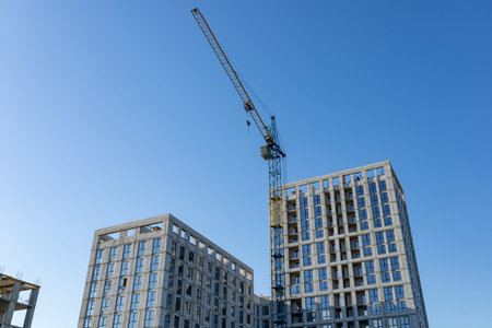 A construction crane lifts materials at a developing high-rise building site surrounded by clear...