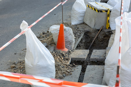 Excavation work is underway in a city street, surrounded by safety barriers and construction materials. The area is cordoned off for safety.の写真素材