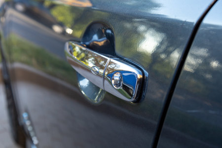 The car door handle reflects sunlight in a suburban neighborhood with blurred greenery in the background, showcasing its chrome finish.の写真素材