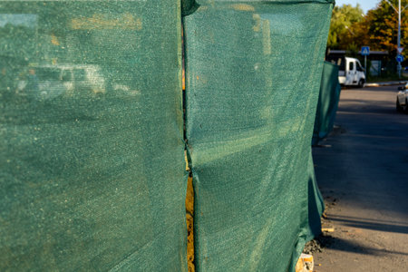 Workers are completing a construction project behind green mesh fencing on a bustling city street in...