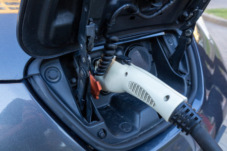 An electric vehicle is hooked up to a charging station in a city neighborhood, taking advantage of...