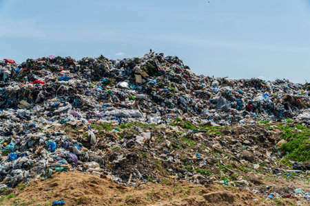Vast outdoor landscape showing a towering mound of assorted plastic waste and discarded trash under...