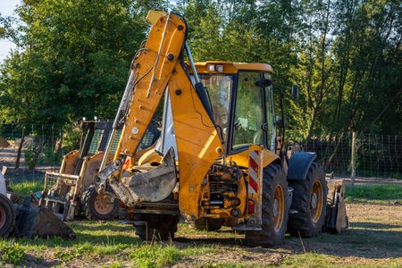 Large yellow powerful backhoe loader parked outdoors on a construction site. Heavy machinery with...