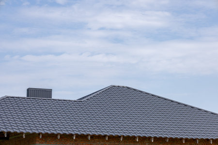 Modern house roof with dark grey tiles, featuring a chimney and brick wall. New residential building...