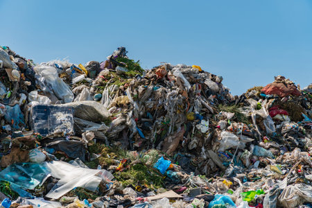A large mound of garbage sits under a clear blue sky, showcasing the significant waste problem...