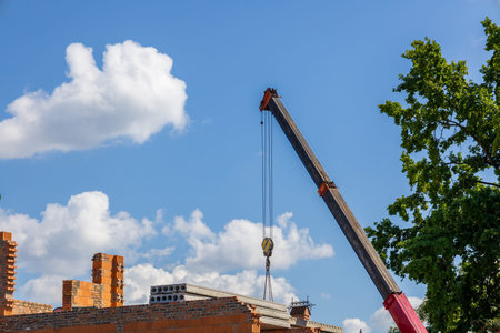 A crane is lifting construction materials at a residential building site on a sunny day with...