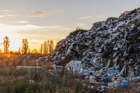 A massive accumulation of trash and waste is piled high at a landfill as the sun sets, highlighting the severe pollution and ecological impact.の写真素材
