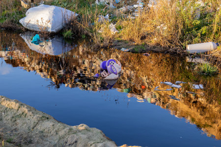 A waterway with dark, polluted water reflects garbage and waste along its banks, highlighting significant environmental issues.の写真素材