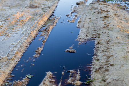 Dark, polluted water collects in a dirt pathway, highlighting the ongoing issue of environmental pollution from waste.の写真素材
