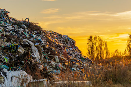 A sunset highlights a landfill filled with plastic debris and rubbish, illustrating the impact of waste on the environment and ecology.の写真素材