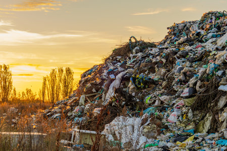 A large landfill site filled with garbage and waste is highlighted against a beautiful sunset,...