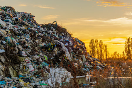 A vast landfill filled with garbage and waste sits under a vibrant sunset sky, highlighting the impact of pollution on the environment.の写真素材