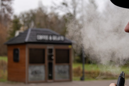 A person is smoking near a cozy outdoor cafe, creating clouds of vapour in a serene autumn setting...